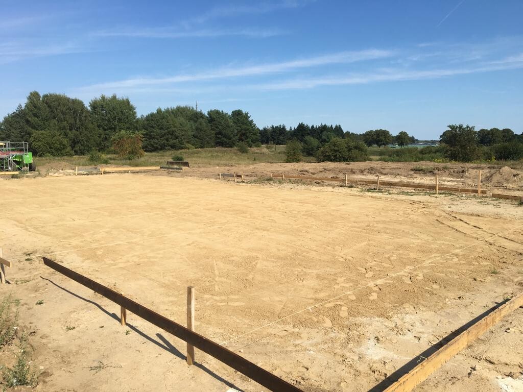 Baustelle mit vorbereitetem Fundament, Sandboden und Holzrahmen am Rand