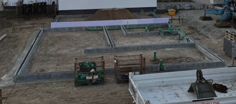 Baustelle mit Fundamentgräben, Betonplatten, Stahlrahmen, Baumaschinen und Lagermaterialien