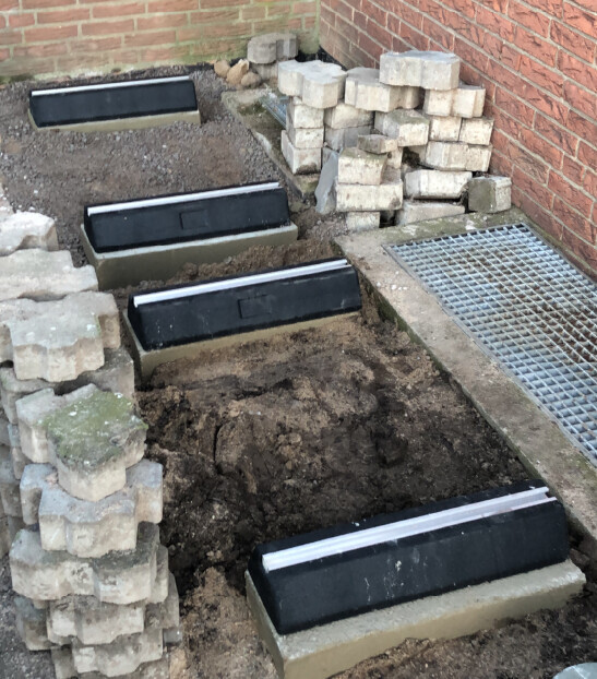Baustelle: schwarze Betonstufen in einer Baugrube, daneben gestapelte Pflastersteine und Gitterrost.