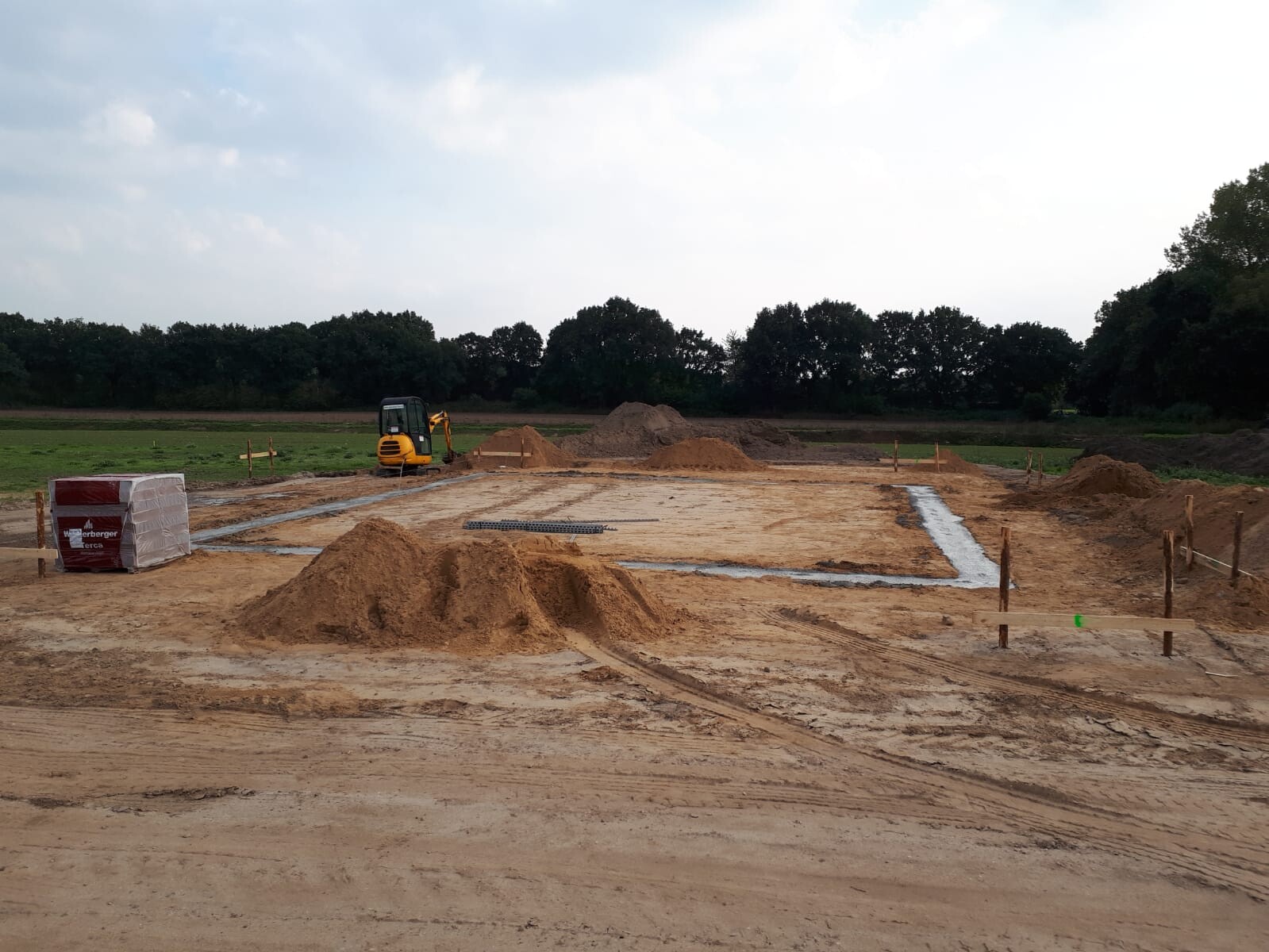 Baustelle mit Bagger, Sandhaufen und Fundamentgraben auf freiem Feld