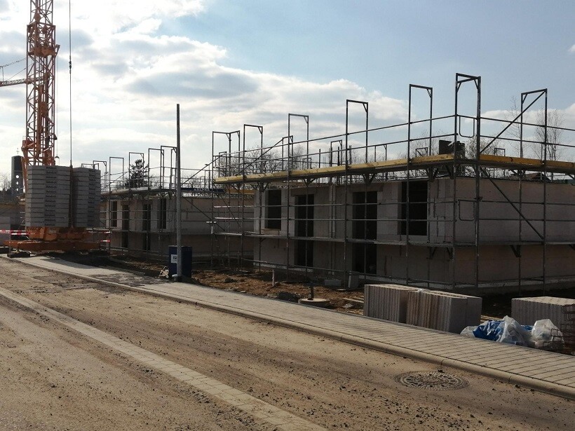 Baustelle mit Gerüstkonstruktionen, halbfertiges Gebäude, linker Kran, Baumaterialien am Boden.