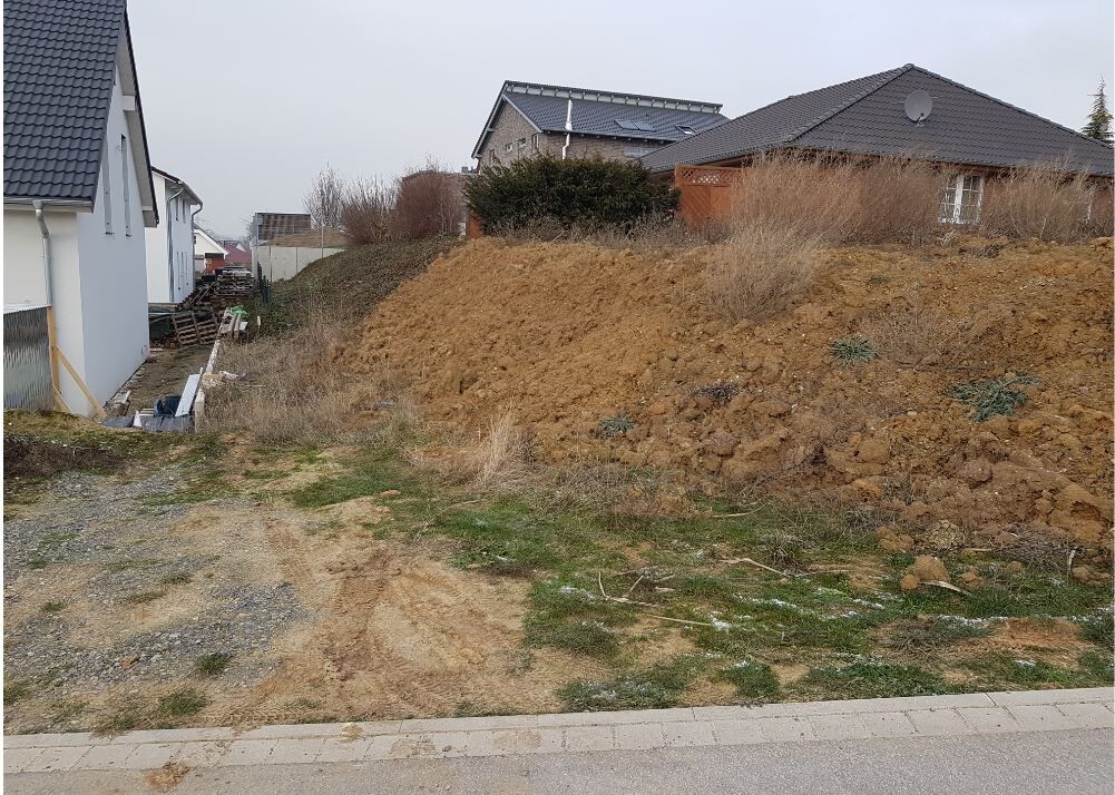 Baugrundstueck mit grosser Erdmulde, Baumaterialien links neben Wohnhaus.