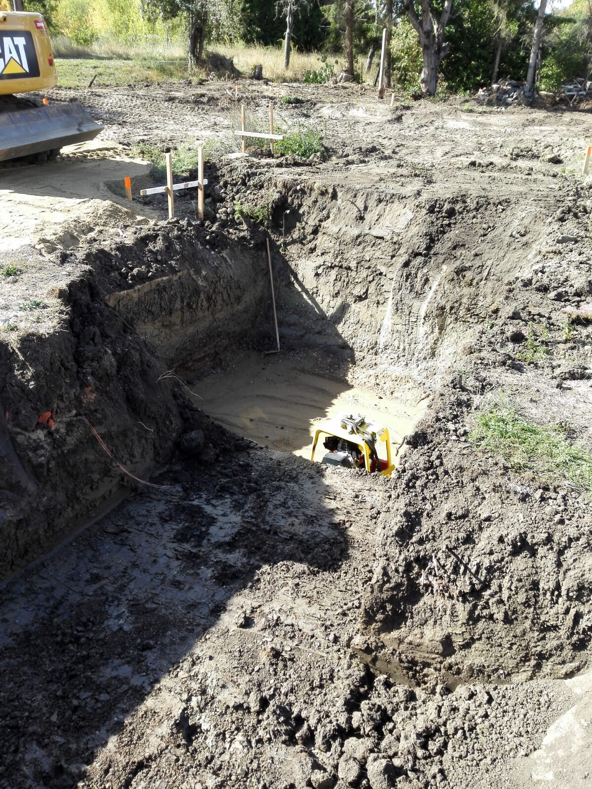 Tiefbau-Baugrube auf Baustelle mit Bagger und Holzpfosten