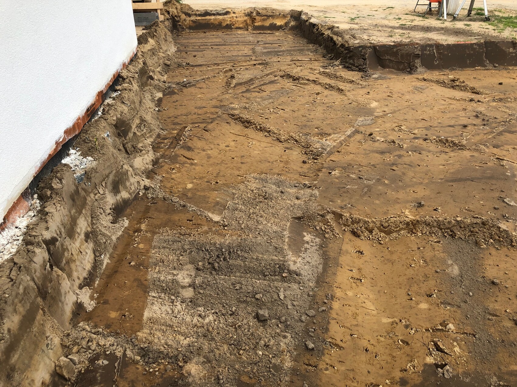 Baustelle: Graben neben der Hauswand, freigelegtes Fundament und Erdreich sichtbar.