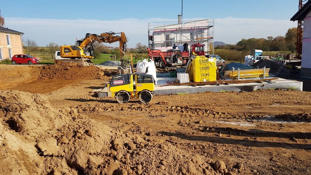 Baustelle mit Bagger, Erdehaufen und Baugeräten beim Fundamentbau