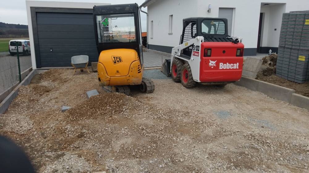 Baustelle mit gelbem JCB-Minibagger und rotem Bobcat vor Neubau