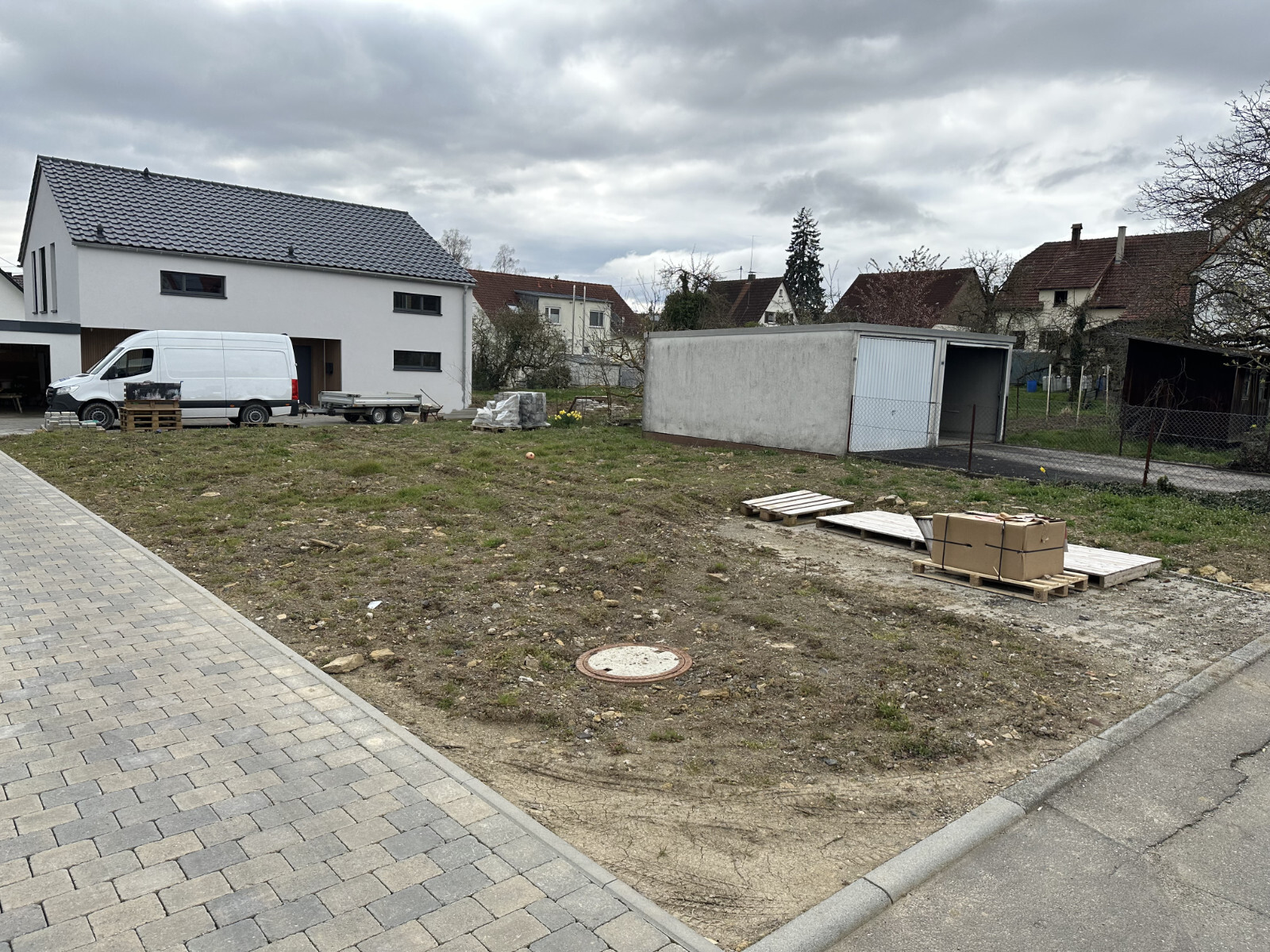 Baustellengrundstück mit weißem, modernem Haus, Van, Paletten und Bauholz; Wolkenhimmel.