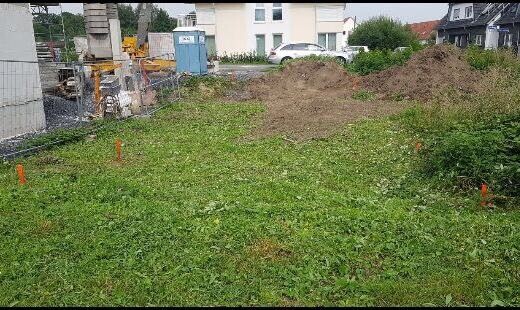 Baugrundstück mit Gras, Erdarbeiten, Erdhaufen und Baucontainer im Hintergrund