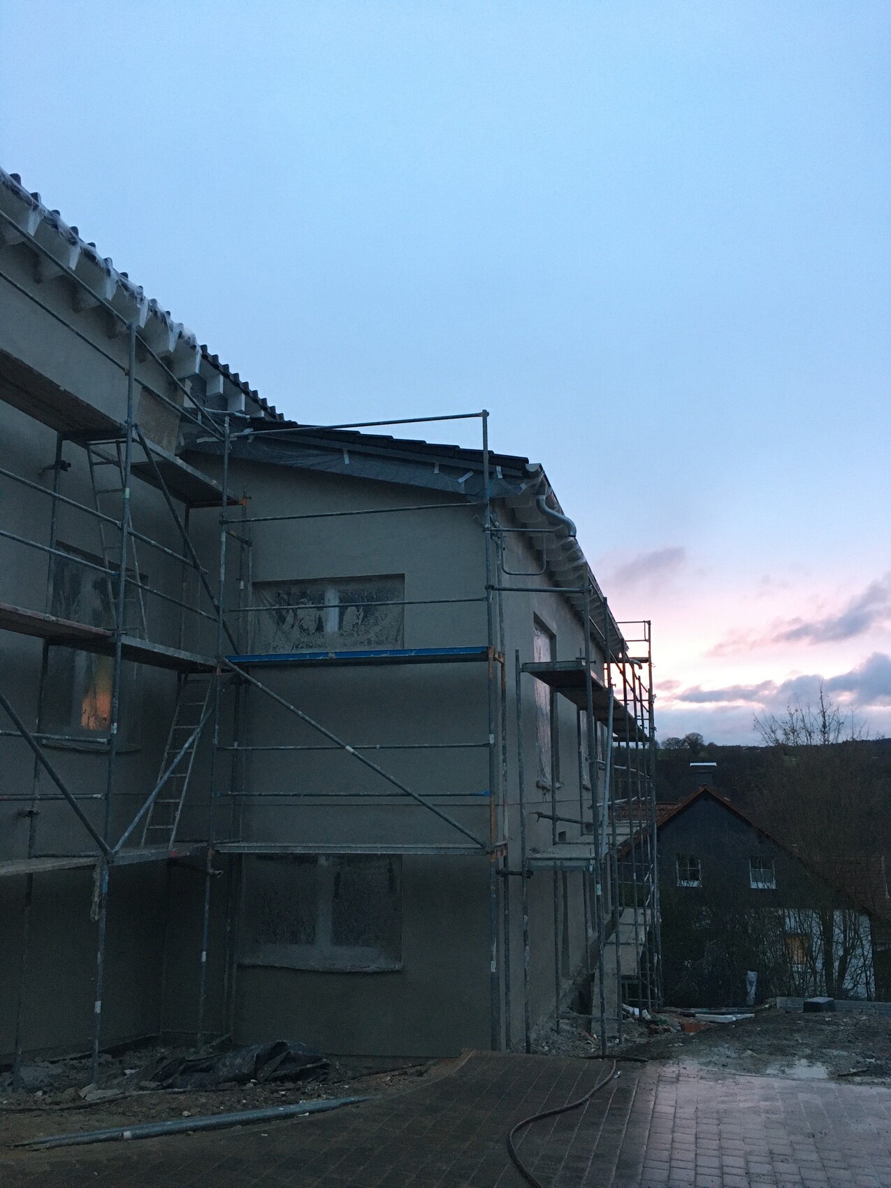 Mehrstöckiges Haus im Bau mit Gerüst entlang der Fassade bei Dämmerung.