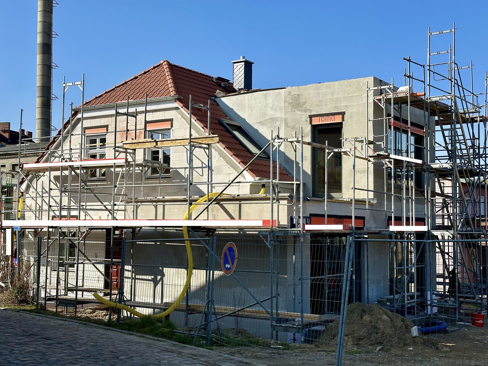 Wohnhaus im Bau mit Gerüsten, Bauzaun und gelben Rohren