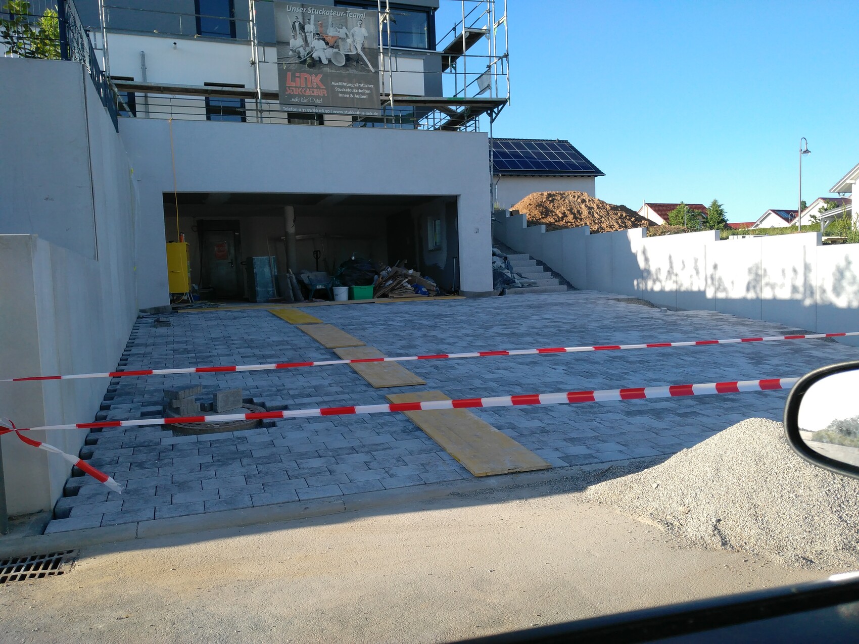 Pflasterte Einfahrt einer Baustelle mit Absperrband, Baumaterialien und Sandhaufen
