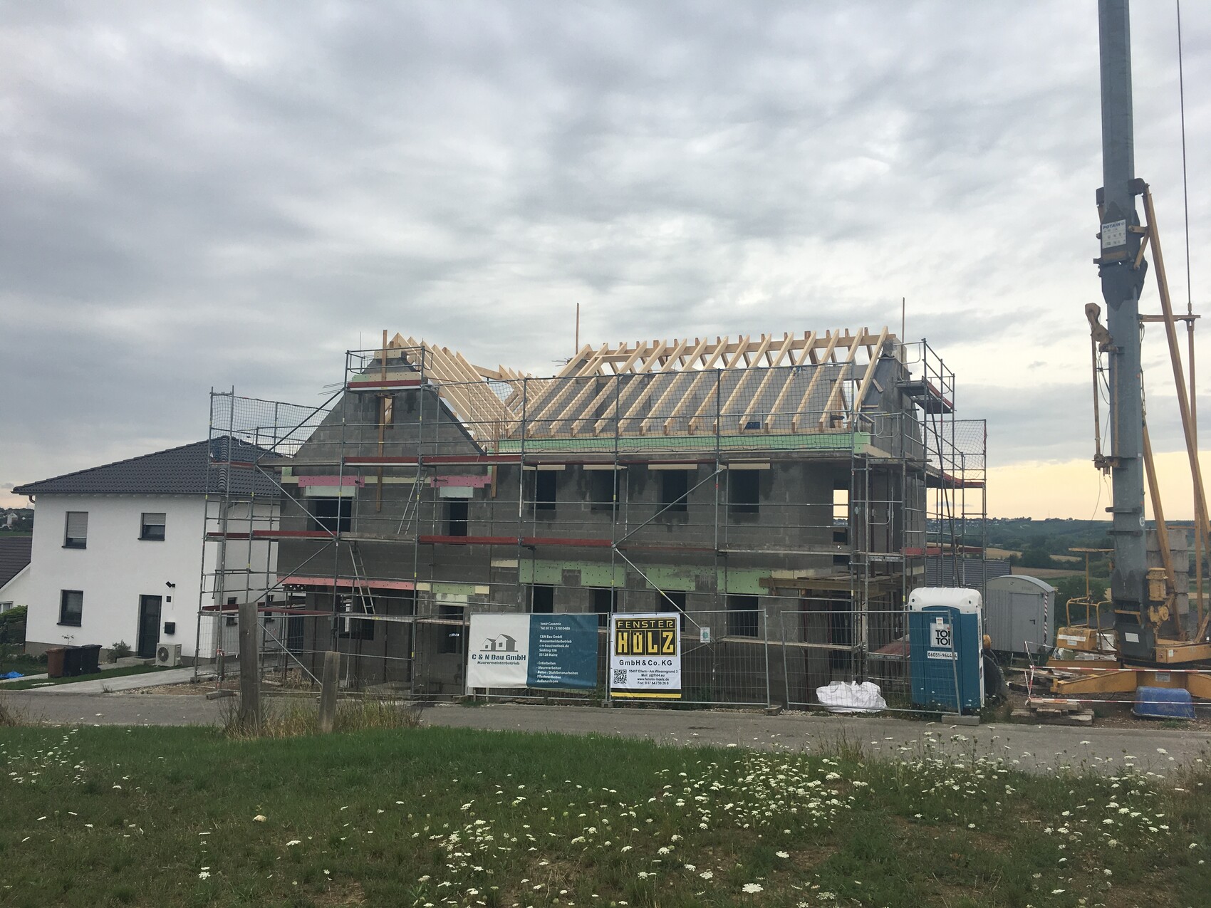 Rohbau eines mehrstöckigen Hauses mit Dachkonstruktion aus Holz, Gerüst und Kran rechts.