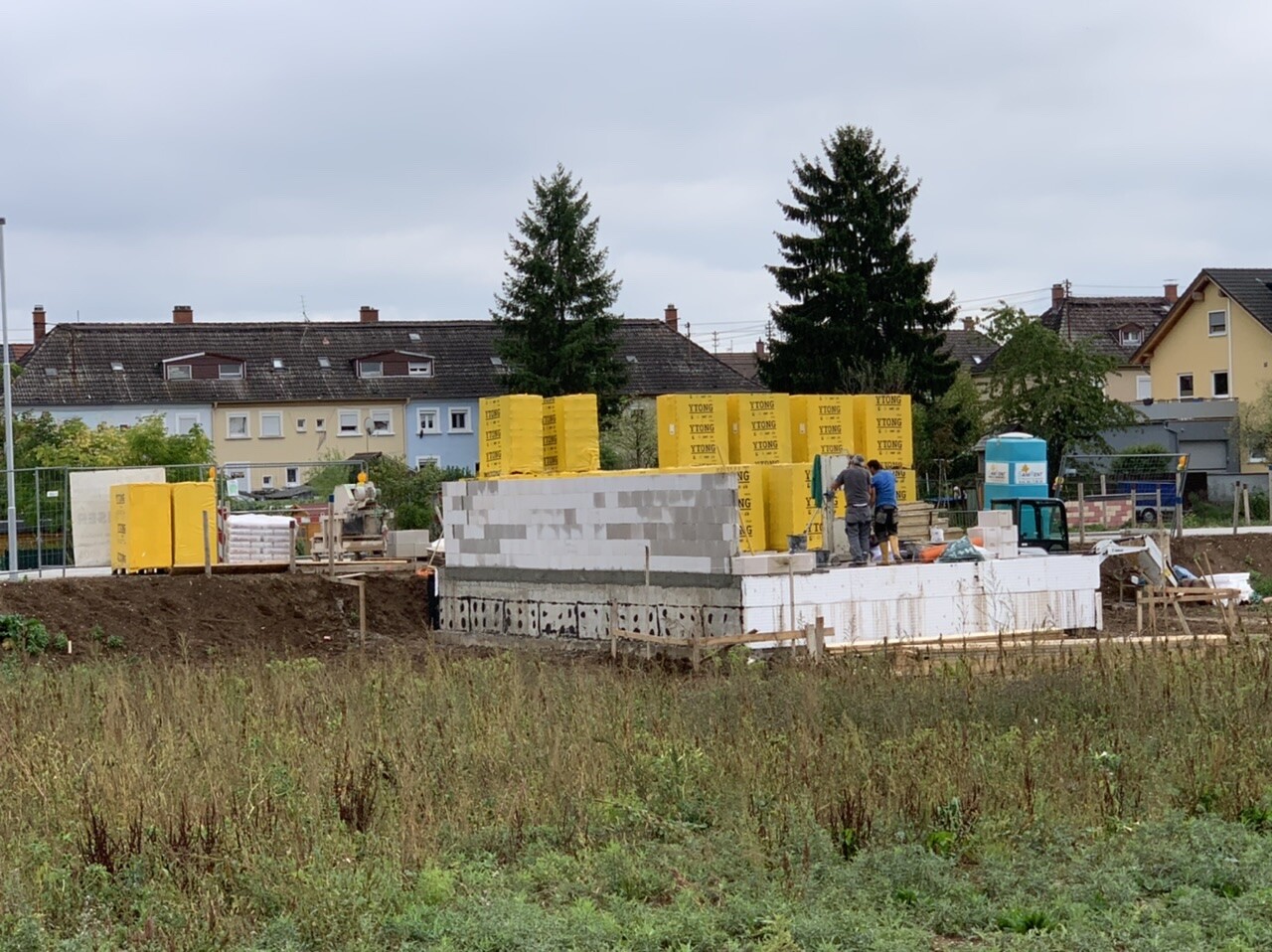 Baustelle mit gelben YTONG-Steinen, Bauwand aus Beton, zwei Arbeiter, Hintergrundhäuser