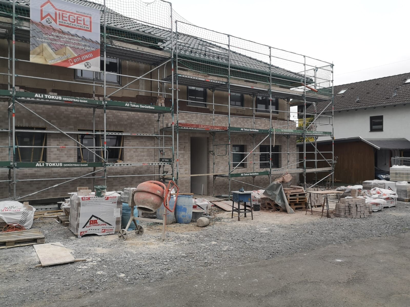 Baustelle am Gebäude: Gerüst um das Haus, Zementmischer, Paletten und Baumaterialien.
