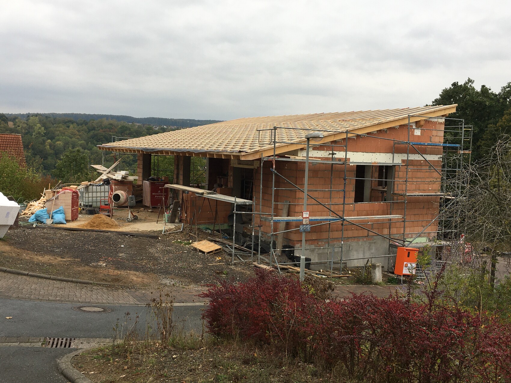 Rohbau eines Hauses mit Gerüst, Holzdachkonstruktion und Baustellenmaterialien.