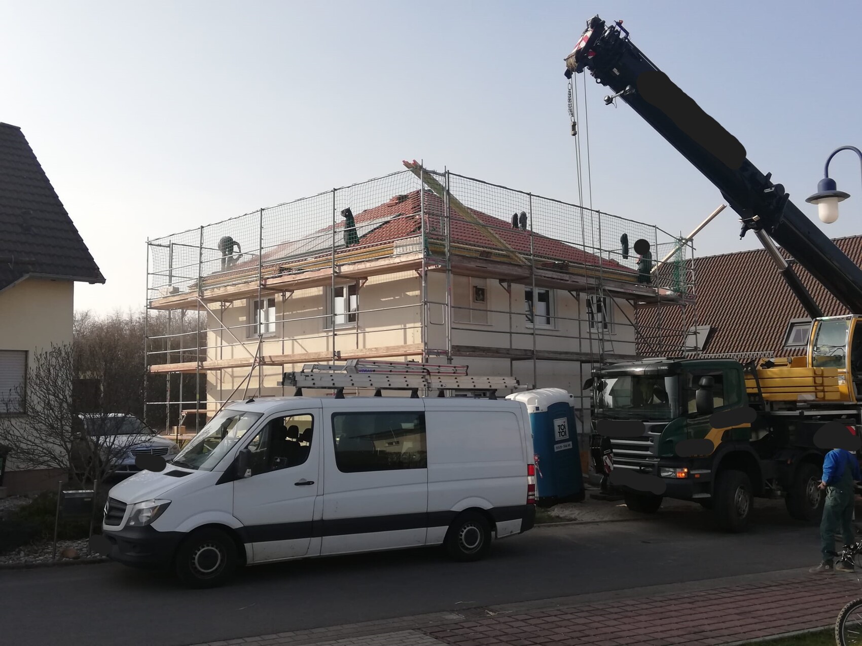 Einfamilienhaus mit Gerüst, Dacharbeiten, Kran und Baufahrzeugen auf der Baustelle
