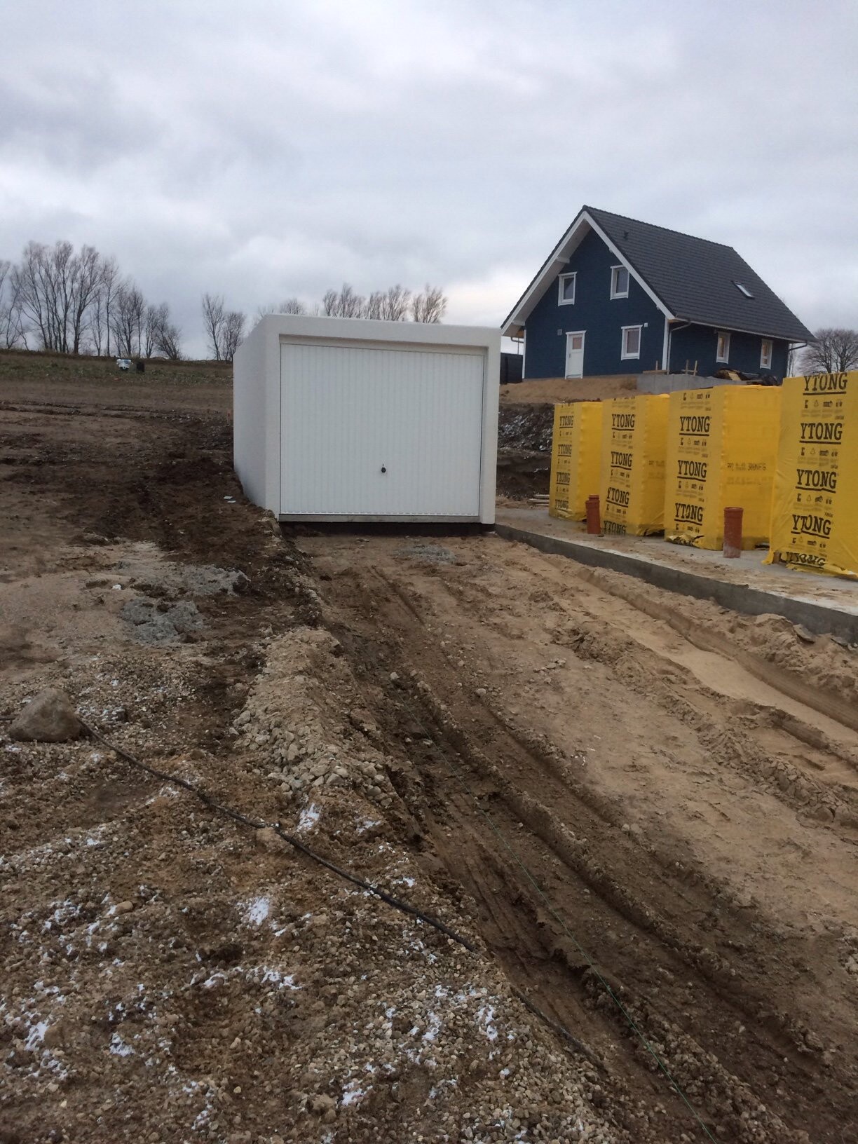 Baustelle mit blauem Haus, gelbe YTONG-Wandbaustoffe und Erdarbeiten im Vordergrund.