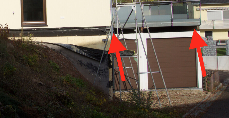 Baustellen-Gerüst vor modernem Haus mit brauner Garage und Glasgeländer.