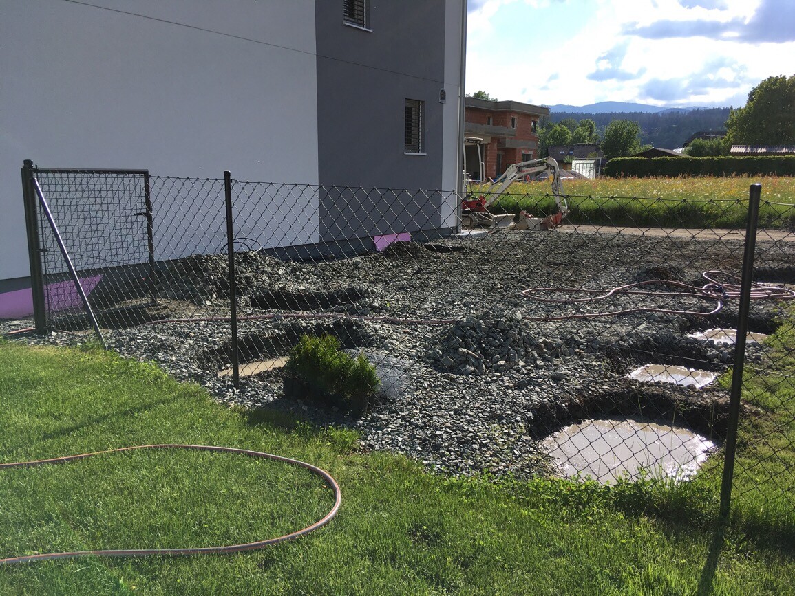 Baustelle am Hausgrundstück mit Graben, Schotter und Bauzaun im Vordergrund