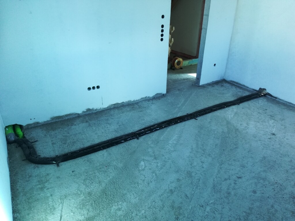Schwarzer Kabelstrang liegt auf rohem Betonboden in einer Baustelle; Türöffnung hinten.