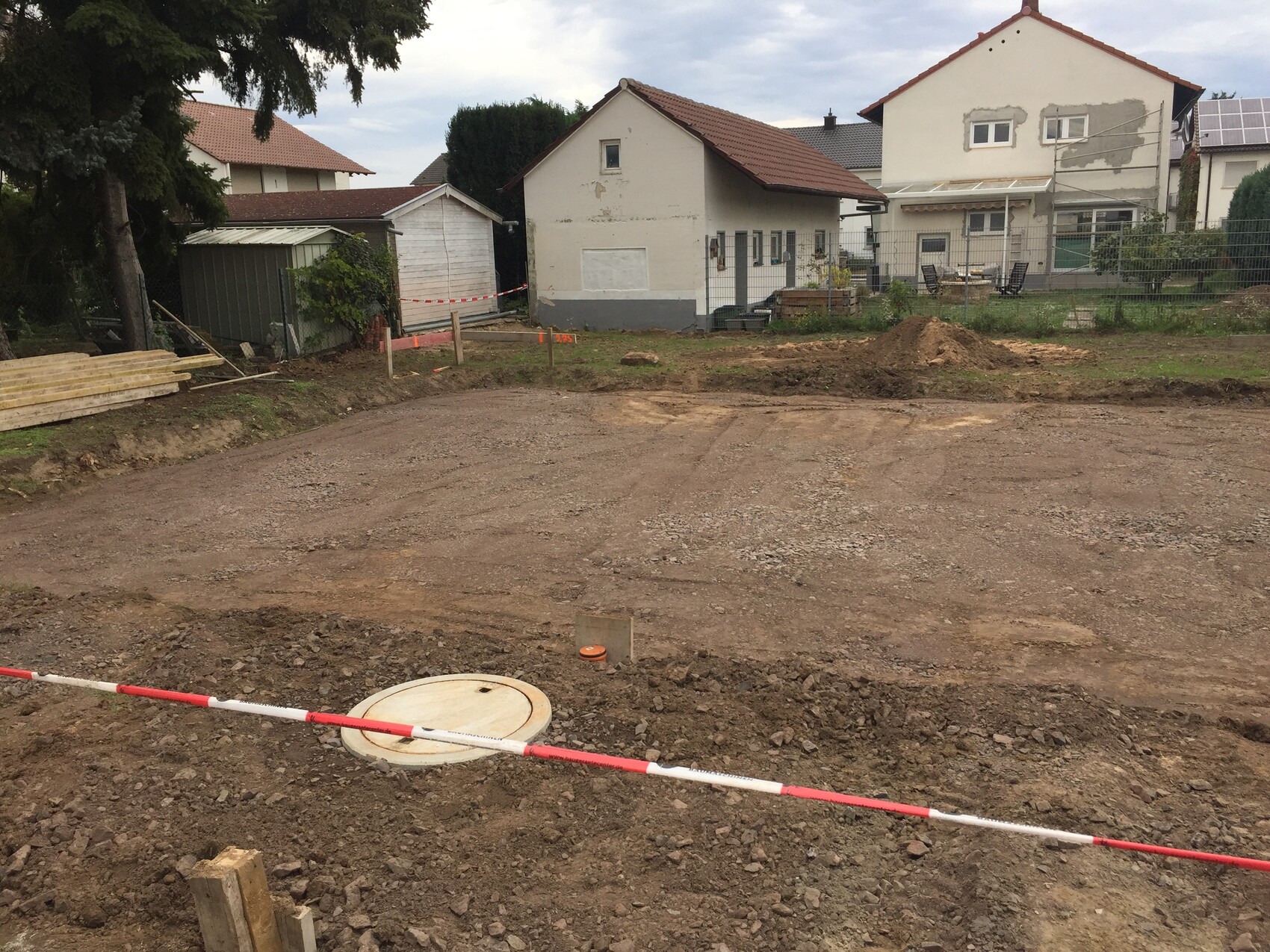 Baugelände mit Erdarbeiten, Absperrband, Materialstapeln und runder Deckel im Vordergrund
