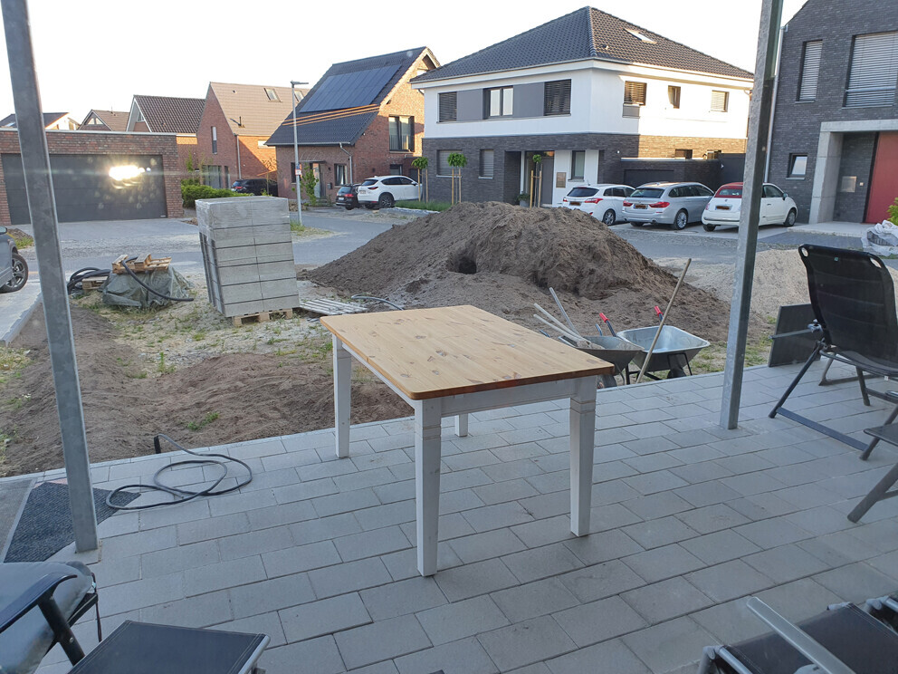 Baustelle in Wohngegend: Holztisch auf Terrasse, Erdhaufen, Baumaterialien, Schubkarren.