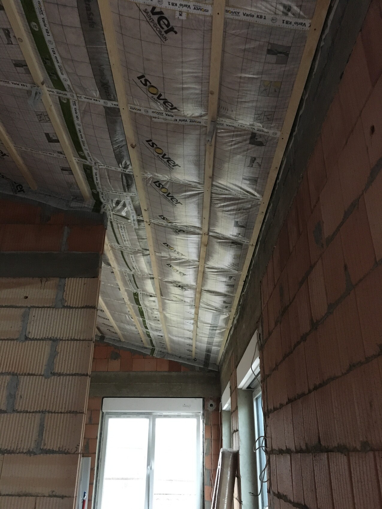Unfertiger Innenraum: Decke mit Holzlatten und Dämmung, Backsteinwände, Fenster am Ende.