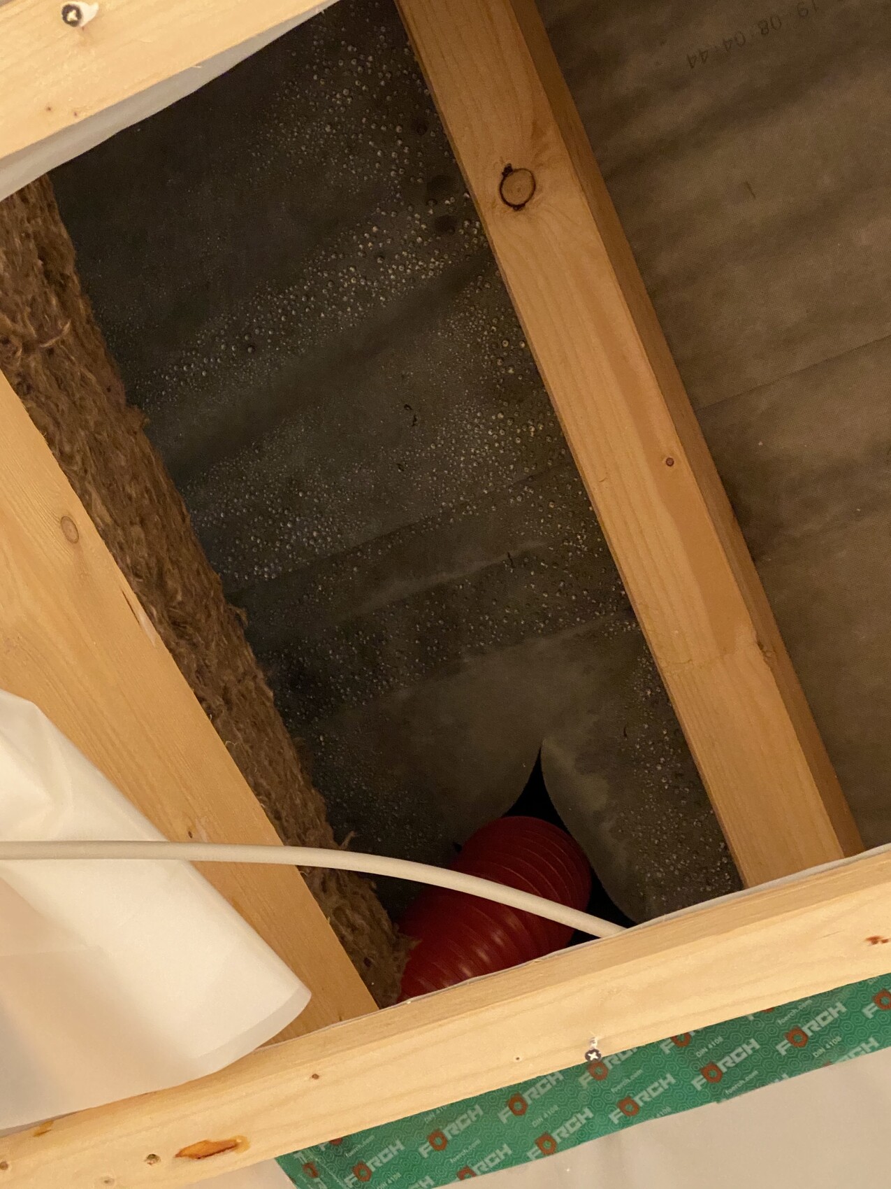 Dachboden-Draufsicht: Holzrahmen, schwarze Dichtfolie, rotes flexibles Rohr, weiße Leitung