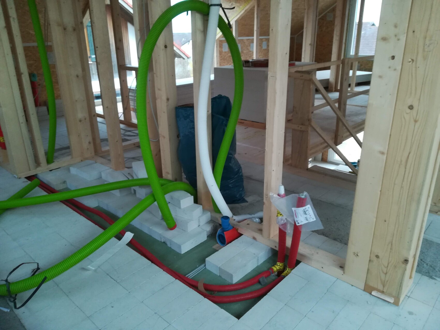 Rohbau: Holzständerwerk, grüne Leitungen, rote Rohre, weiße Styroporblöcke am Boden.