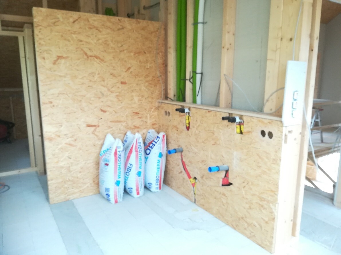 Innenansicht einer Baustelle: OSB-Wand, Rohre und Dämmstoffsäcke.