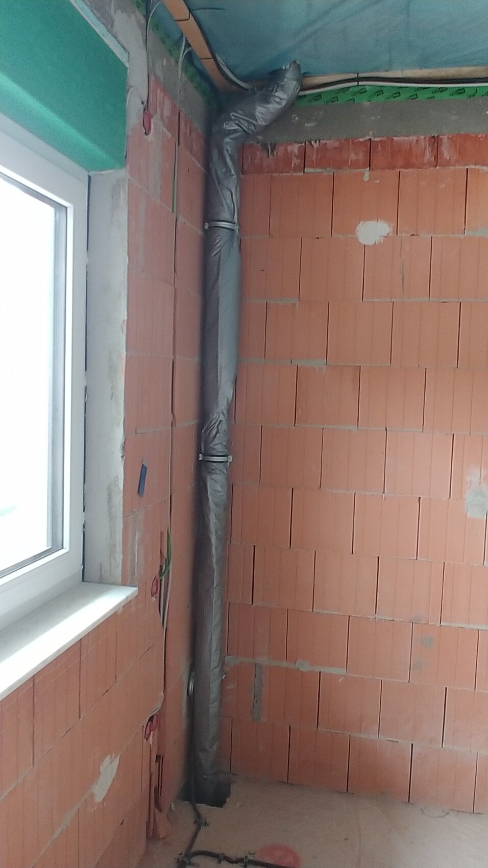 Innenraum einer Bauwohnung mit rotem Ziegelmauerwerk und isolierter vertikaler Rohrleitung.