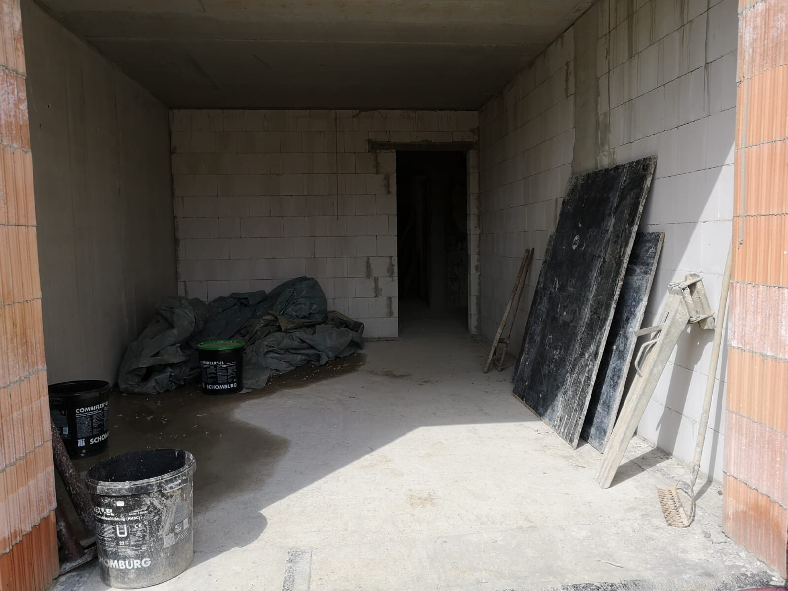Rohbaustelle: unfertiger Innenraum mit Eimern, Planen, Brettern und Werkzeug.