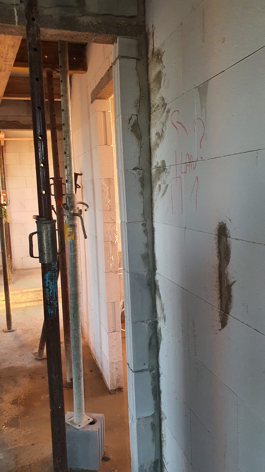 Innenraum einer Baustelle mit Gerüstpfosten, Betonwänden und Wandmarkierungen.