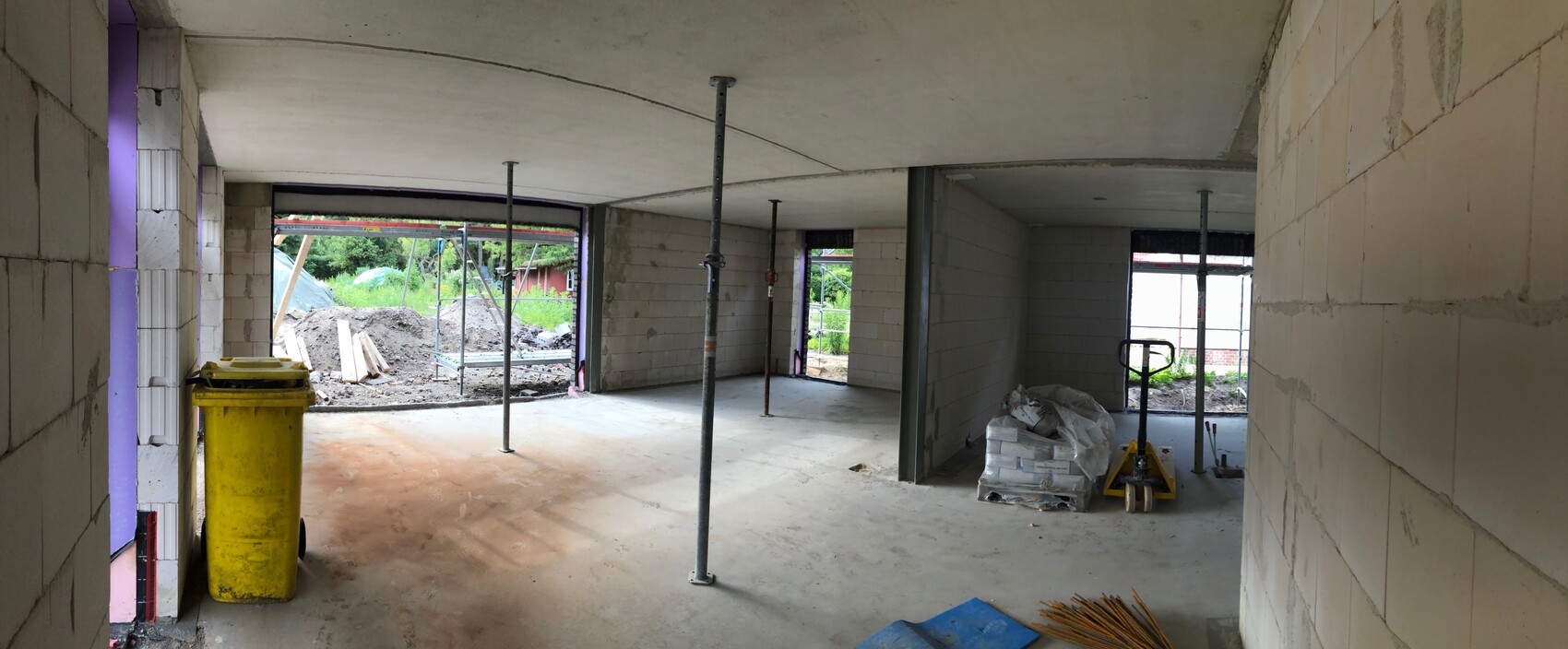Unfertiger Innenraum einer Baustelle: Stützen, Baumaterial und Blick nach außen.