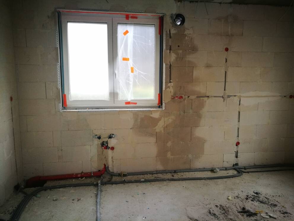 Baustelle Innenraum mit Fenster, unverputzten Wänden und sichtbaren Wasserleitungen.