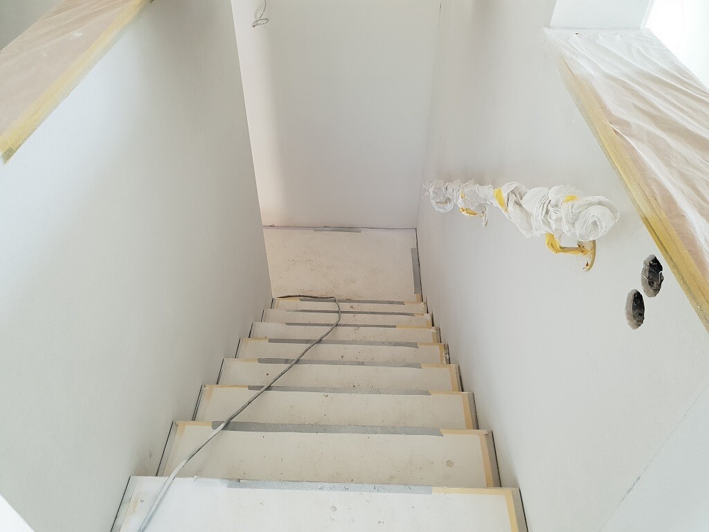 Renoviertes Treppenhaus mit Abdeckfolien an den Wänden und sichtbaren Kabeln entlang der Treppe.