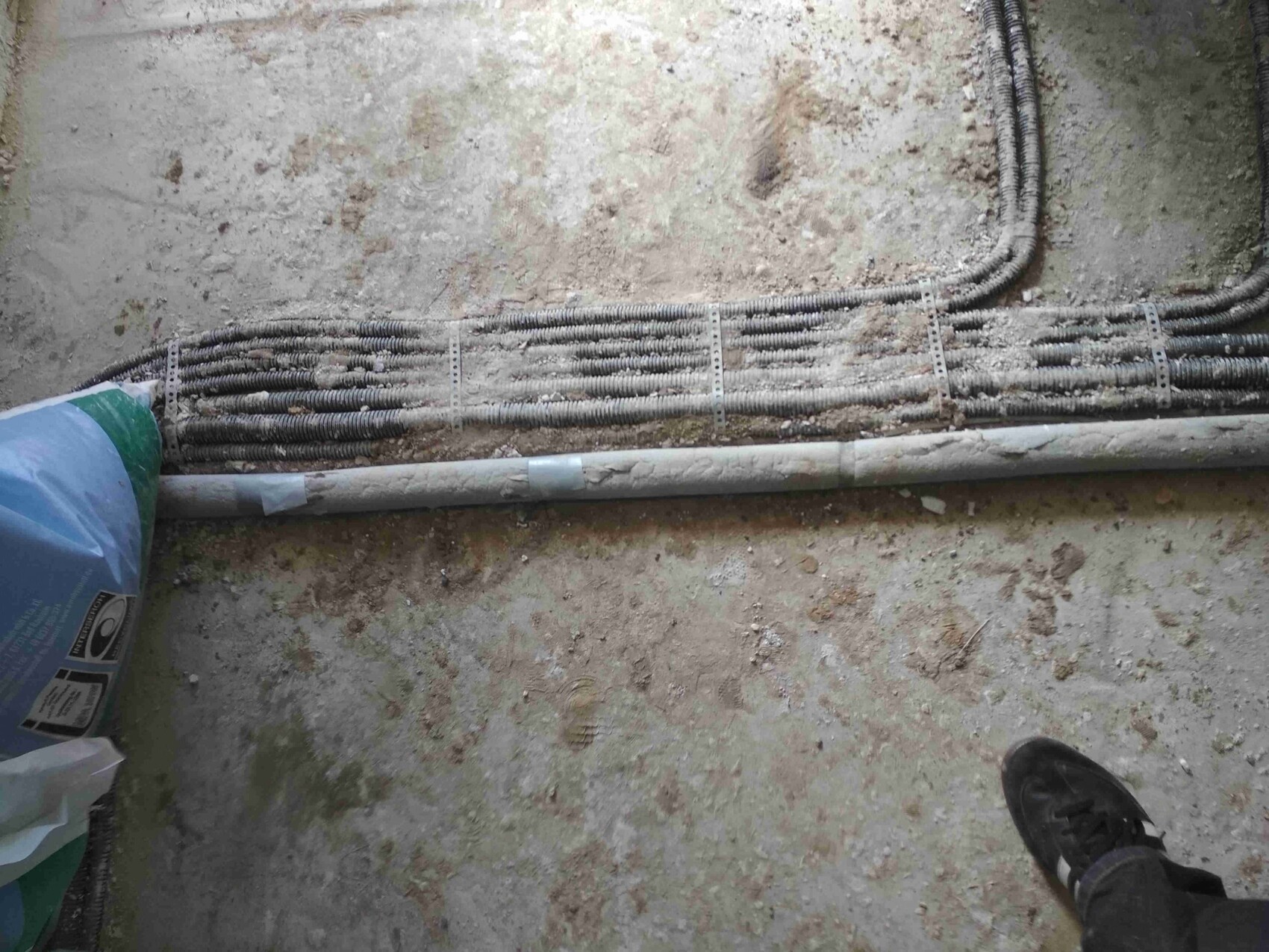 Baustelle mit verlegten Kabelrohren auf dem Boden, Schuh im unteren Rand sichtbar