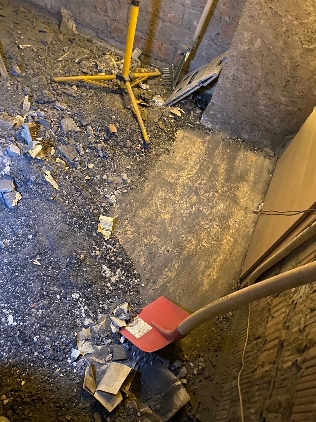 Kellerbaustelle: Schutt, Staub, gelbes Stativ, rote Schaufel, Backsteinwand.