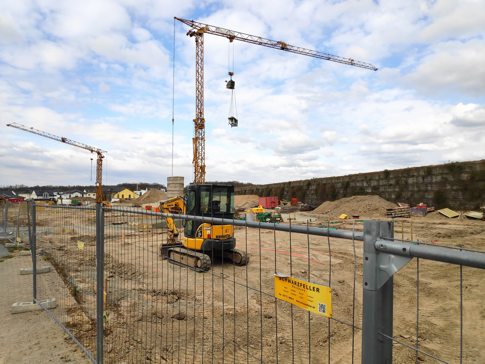 Baustelle mit Kran, Bagger und Bauzäune; Erdaushub, Materialien, Häuser im Hintergrund