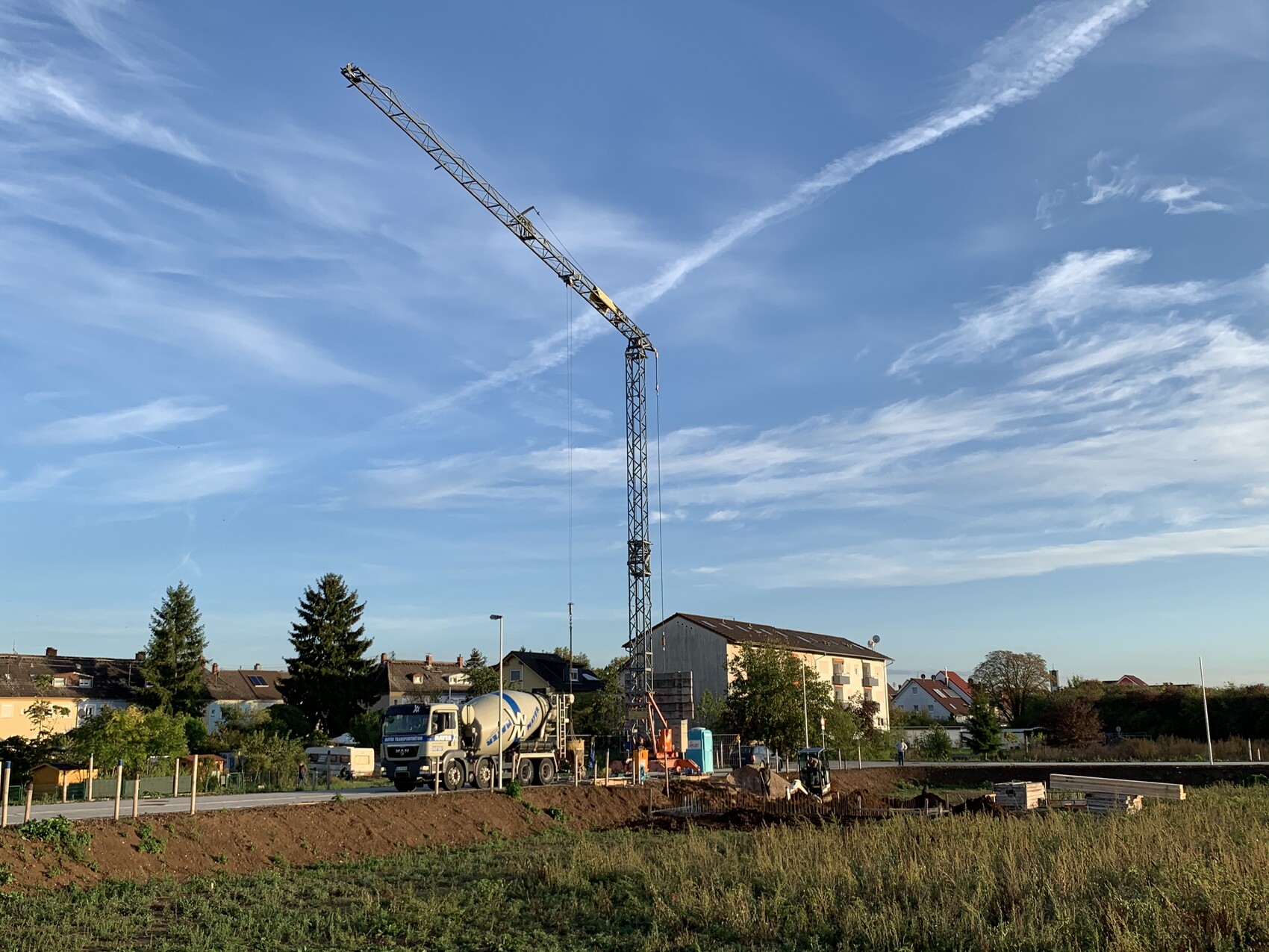 Großer Baukran über einer Baustelle mit Betonmischer, Häuser im Hintergrund.
