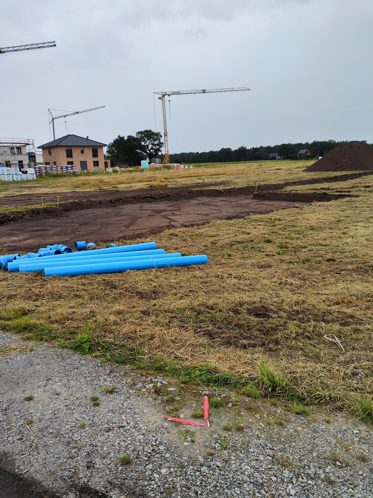 Baustelle mit Kran, Hintergrund Bauarbeiten, blaue Rohre liegen auf dem Gelände.