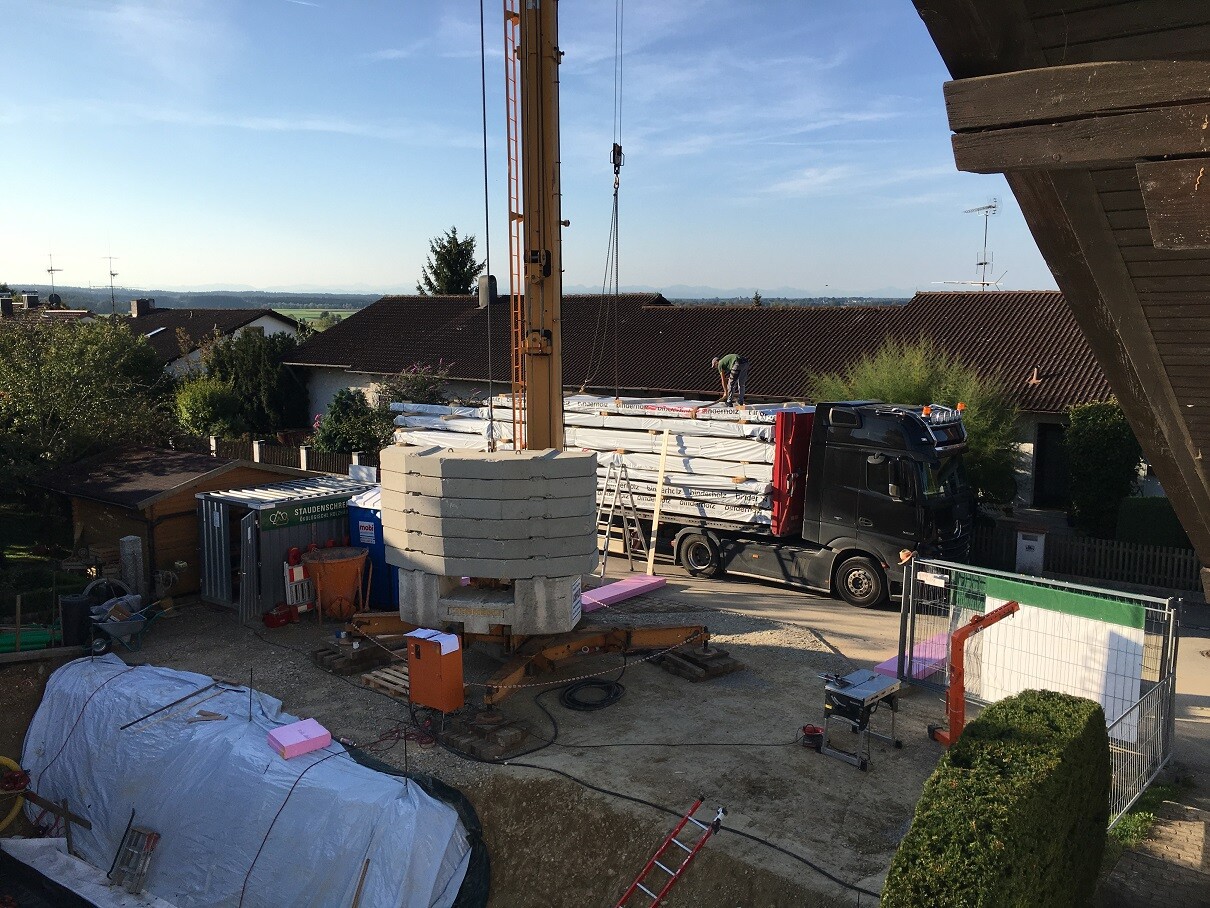Kran hebt Betonblöcke über LKW auf einer Baustelle im Hinterhof eines Wohngebiets.