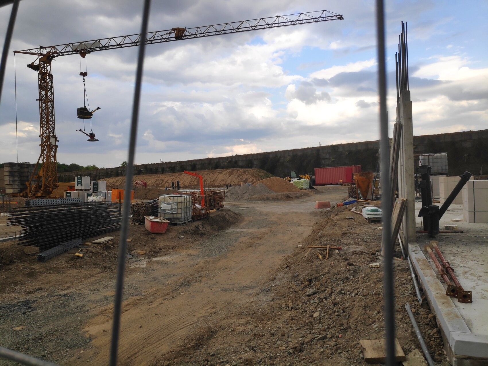 Großer Turmkran auf Baustelle hebt Material; Erde, Paletten und Werkzeuge liegen bereit.