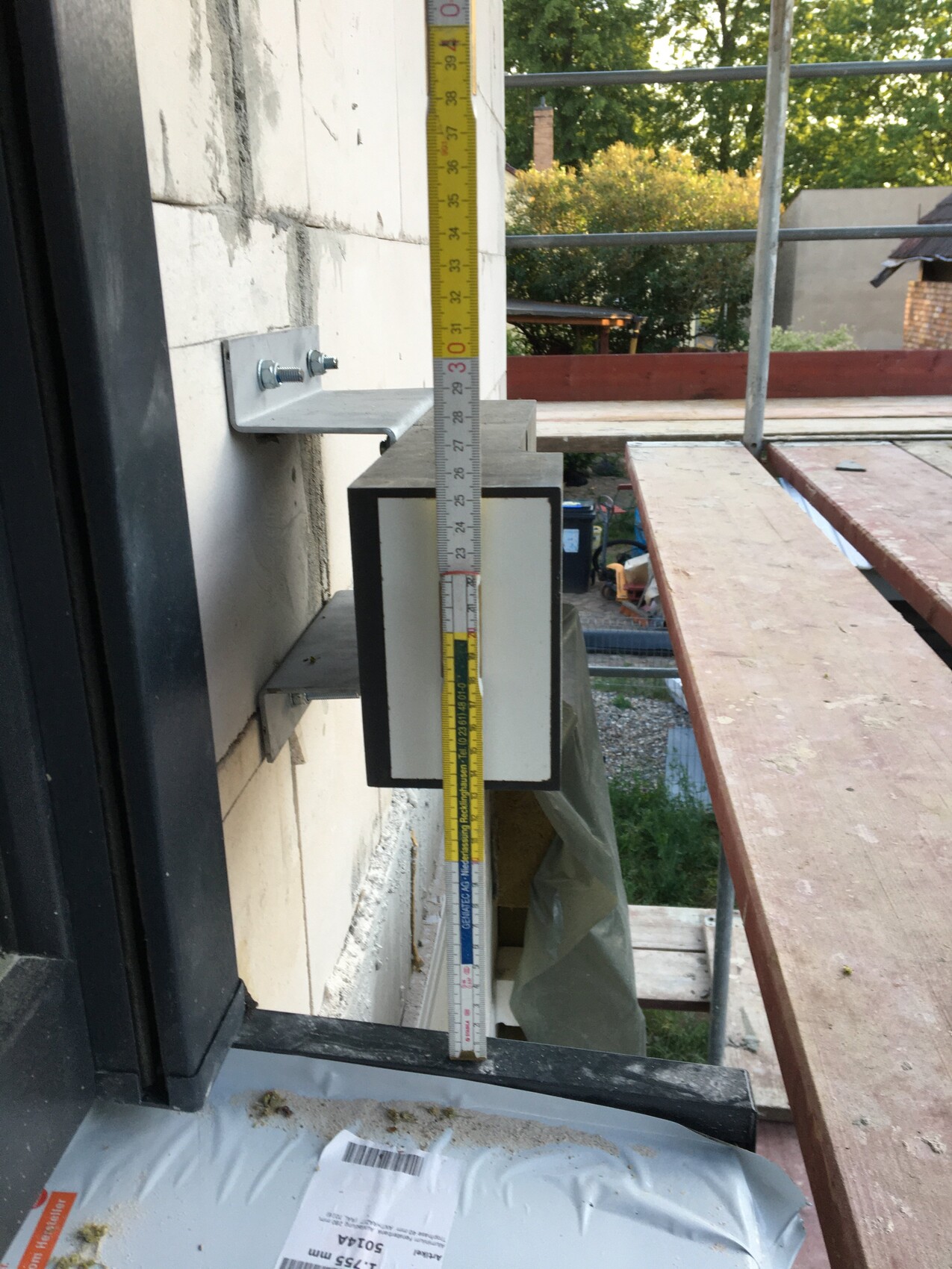 Außenwand mit Wandhalterung und vertikal gespanntem Maßband an einer Baustelle.