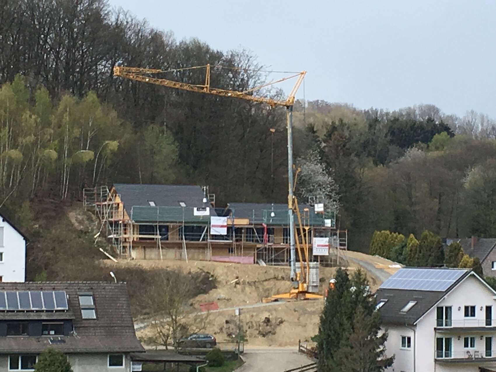 Gelber Baukran über einer Wohnhaus-Baustelle mit Gerüsten und umgebenden Häusern.