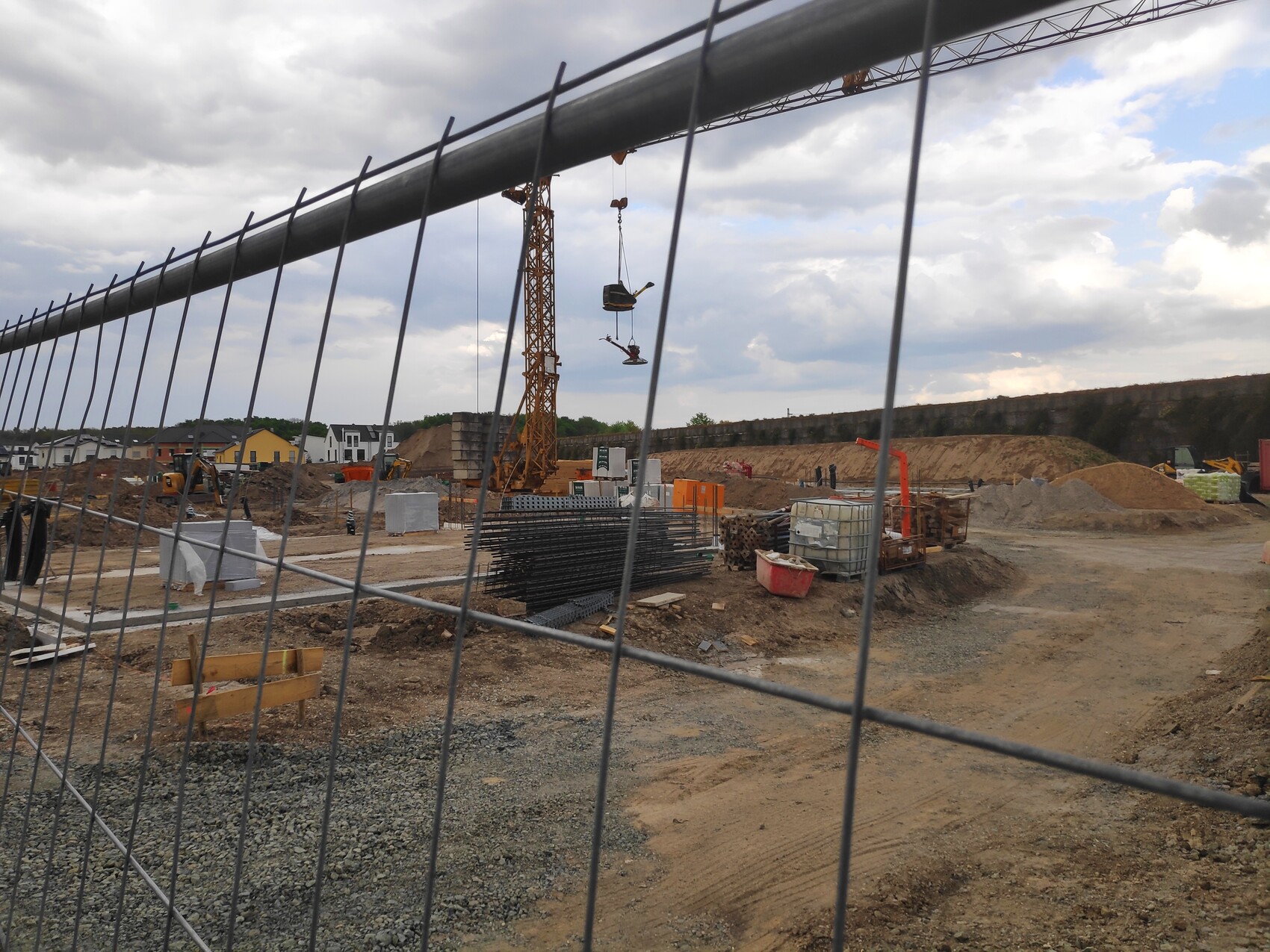 Baustelle mit Kran, Stahlträgern und Baumaterialien; Absperrzaun im Vordergrund.