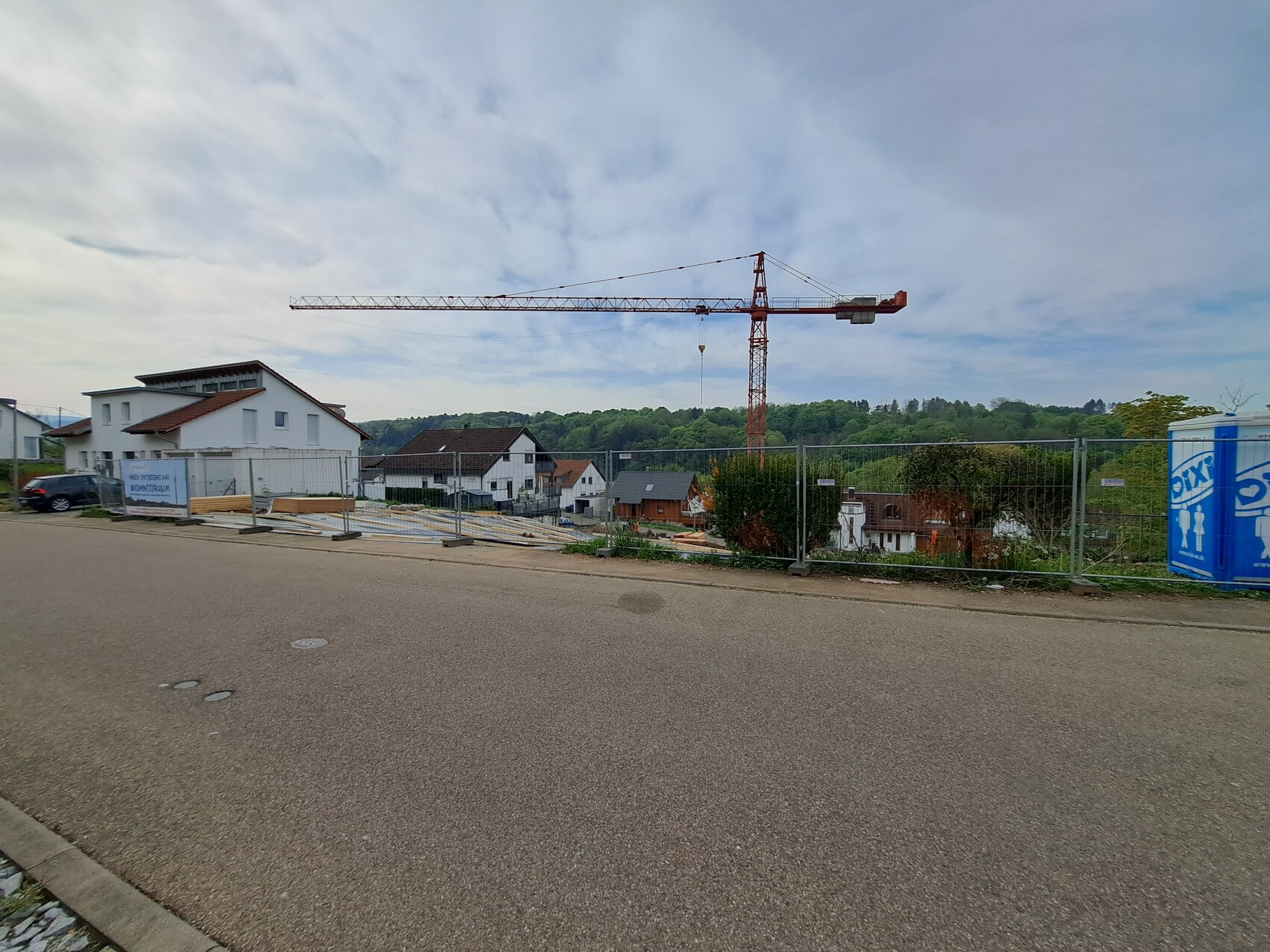 Roter Kran über Wohnbaustelle; Bauzäune, Häuser und Porta-Toilette rechts.