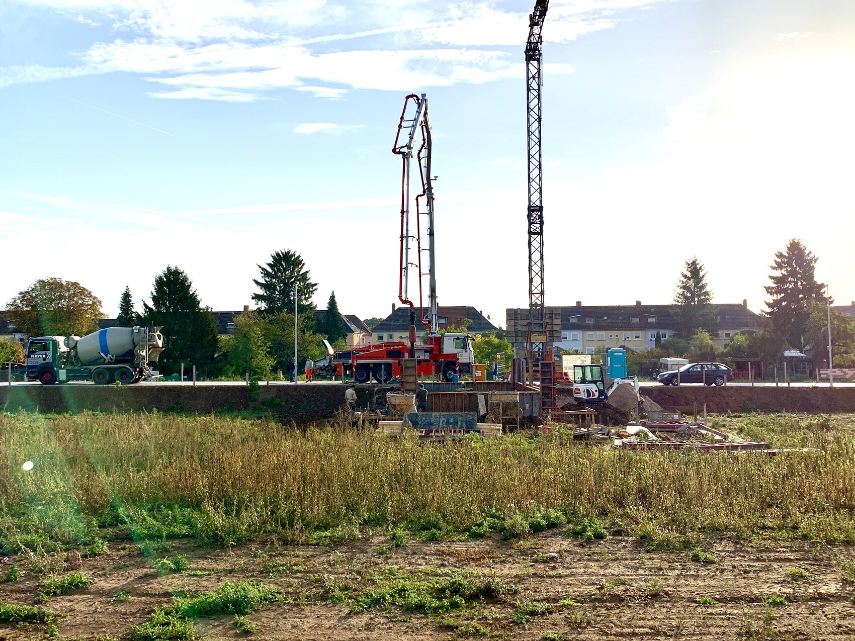 Baustelle mit Kran, Bohranlage und Betonmischer; Hintergrund mit Häusern.