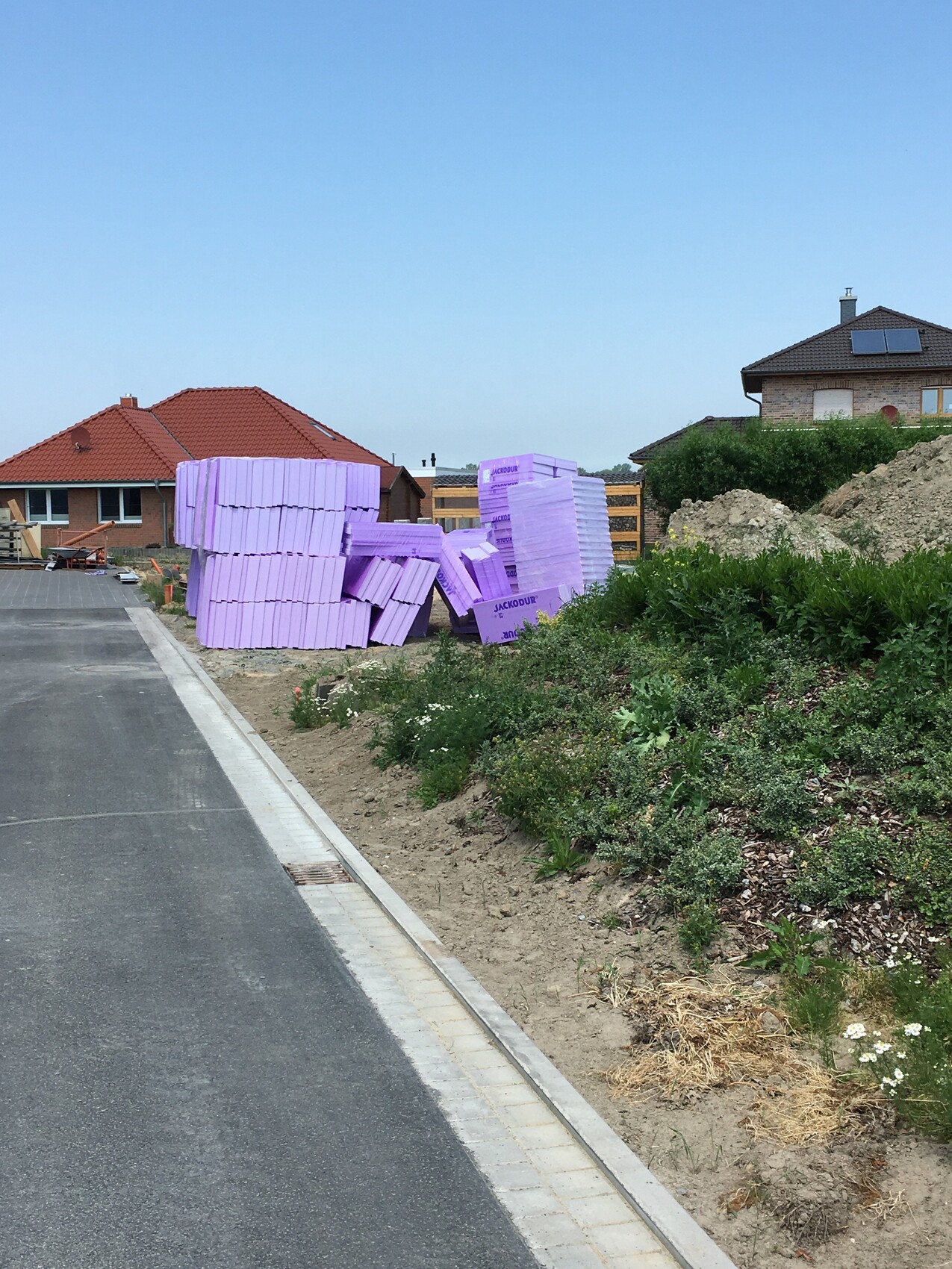 Stapel violetter Dämmplatten aus Polystyrol auf Paletten neben einer Straße auf einer Baufläche.