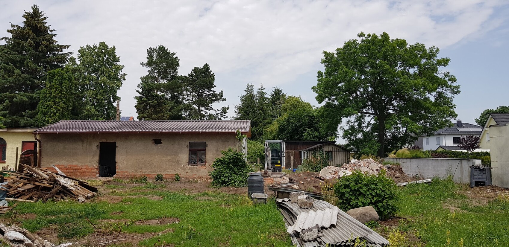 Altes verputztes Einfamilienhaus auf Baugelände; Holz- und Metallabfälle, Bauschutt, Mini-Bagger